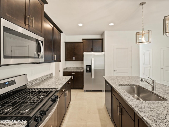 kitchen featuring dark brown cabinetry, pendant lighting, appliances with stainless steel finishes, a sink, and light stone counters