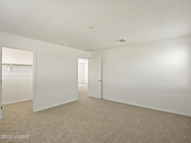 unfurnished bedroom featuring light carpet, baseboards, a spacious closet, visible vents, and a closet