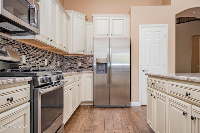 kitchen with backsplash, stainless steel appliances, light wood-type flooring, and light stone countertops