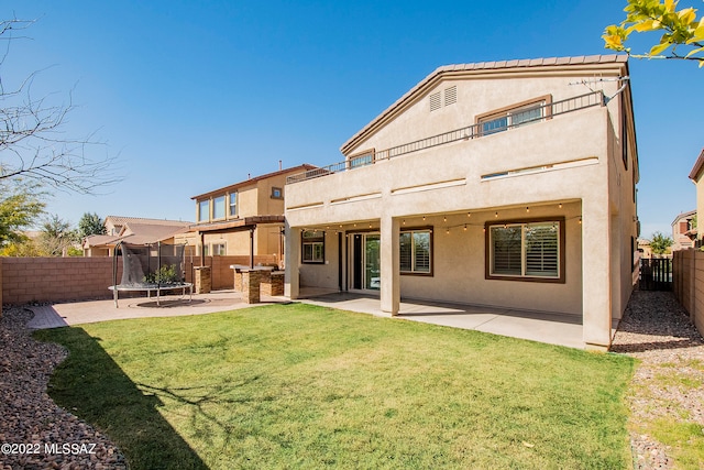 back of property featuring a trampoline, a patio area, and a yard