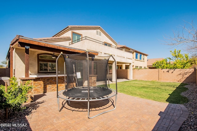 back of property with a trampoline, a patio area, and a yard