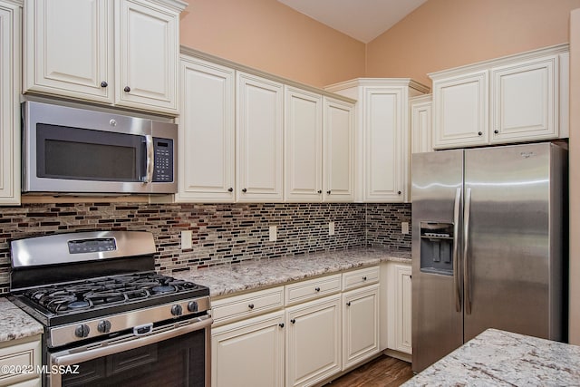 kitchen with stainless steel appliances, dark hardwood / wood-style floors, tasteful backsplash, light stone countertops, and lofted ceiling