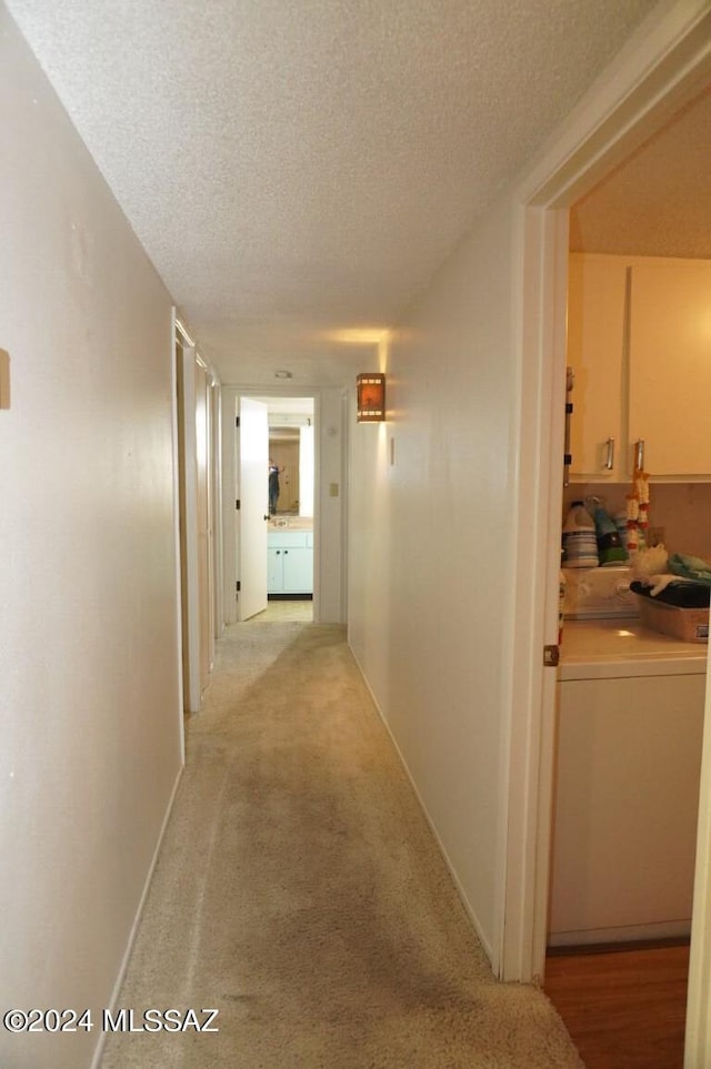 hall with light carpet, washer and dryer, a textured ceiling, and baseboards