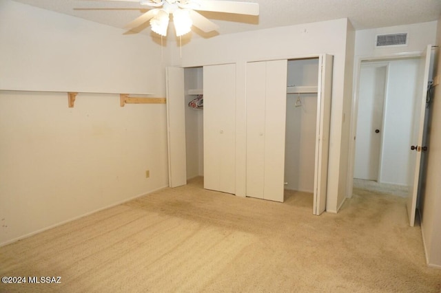 unfurnished bedroom featuring light colored carpet, visible vents, multiple closets, and ceiling fan