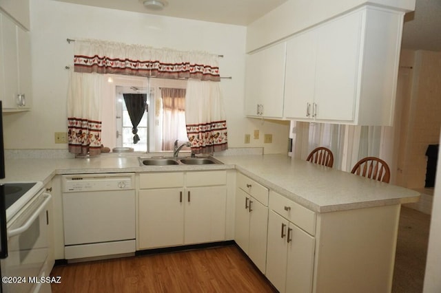 kitchen with white appliances, wood finished floors, a peninsula, a sink, and light countertops