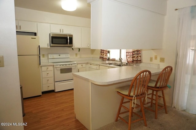 kitchen with light countertops, a peninsula, white appliances, white cabinetry, and a sink