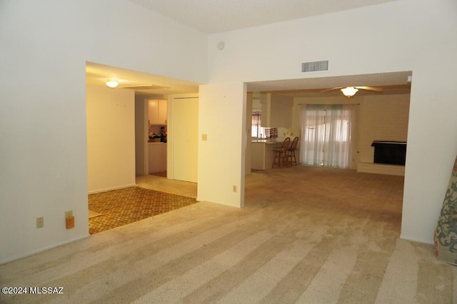 carpeted spare room with a fireplace, visible vents, a towering ceiling, and ceiling fan