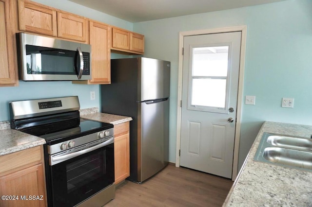 kitchen with light countertops, a sink, appliances with stainless steel finishes, and light wood-type flooring
