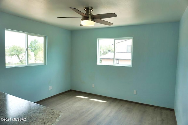 empty room with a ceiling fan, wood finished floors, baseboards, and a wealth of natural light