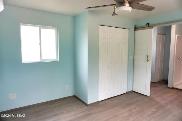 unfurnished bedroom with a closet, a barn door, wood finished floors, and a ceiling fan