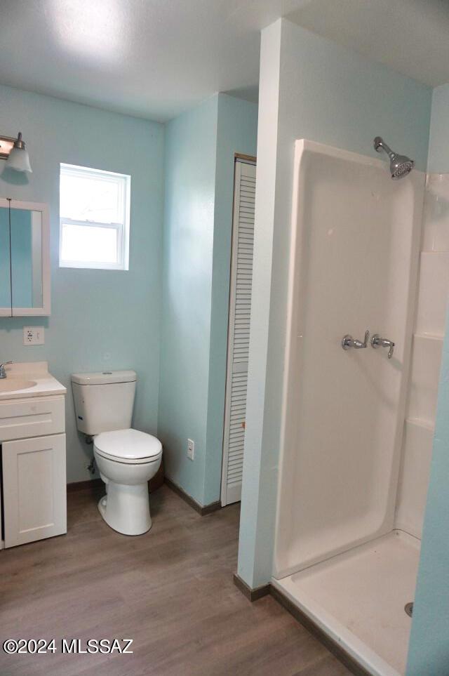 full bathroom with baseboards, wood finished floors, toilet, vanity, and a stall shower