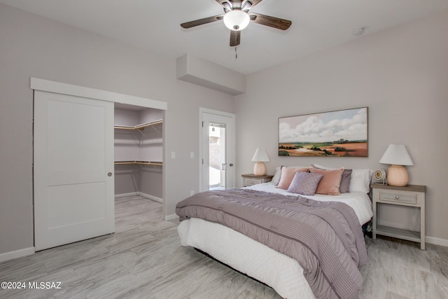 bedroom with baseboards, a ceiling fan, a walk in closet, light wood-style floors, and a closet