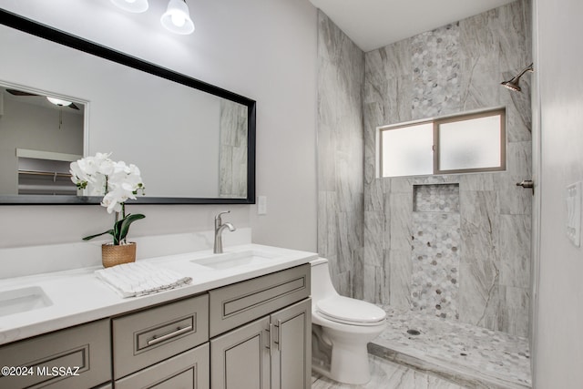 bathroom with toilet, a sink, marble finish floor, a tile shower, and double vanity