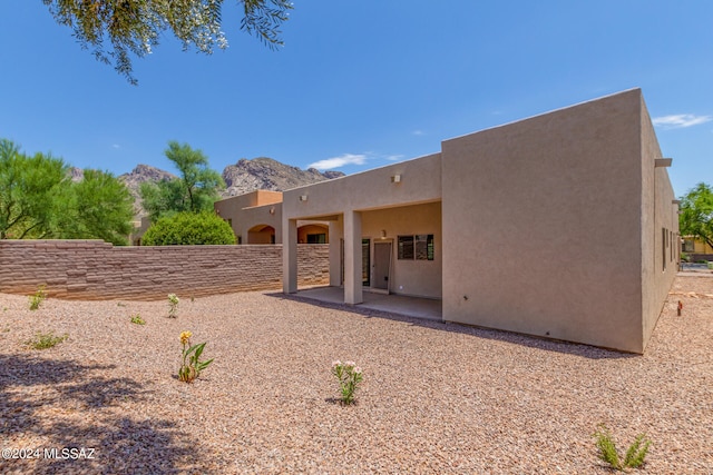 rear view of house with stucco siding, fence, a mountain view, and a patio