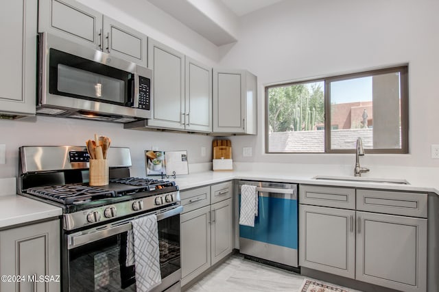 kitchen with gray cabinetry, stainless steel appliances, a sink, and light countertops