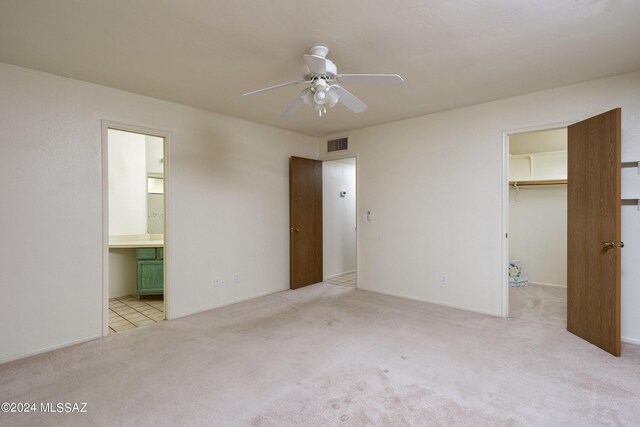 unfurnished bedroom featuring light carpet, ensuite bath, ceiling fan, a spacious closet, and a closet