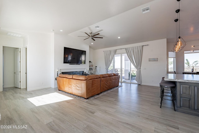 living area with lofted ceiling, a glass covered fireplace, visible vents, and light wood-style floors