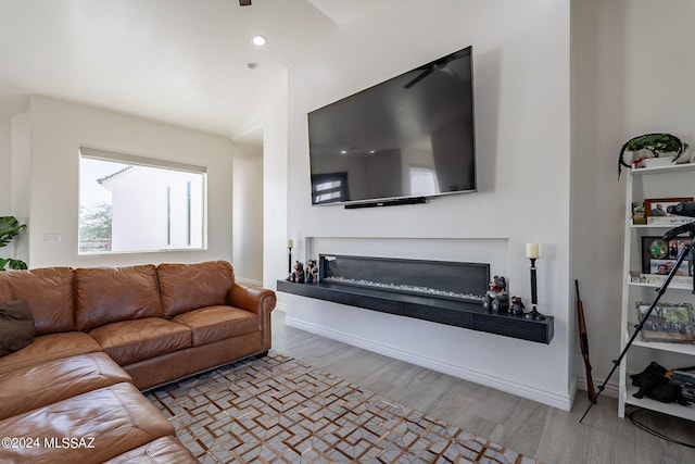 living room with baseboards, vaulted ceiling, wood finished floors, and a glass covered fireplace