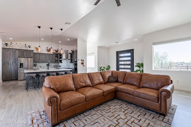 living area featuring light wood-style floors, visible vents, and vaulted ceiling