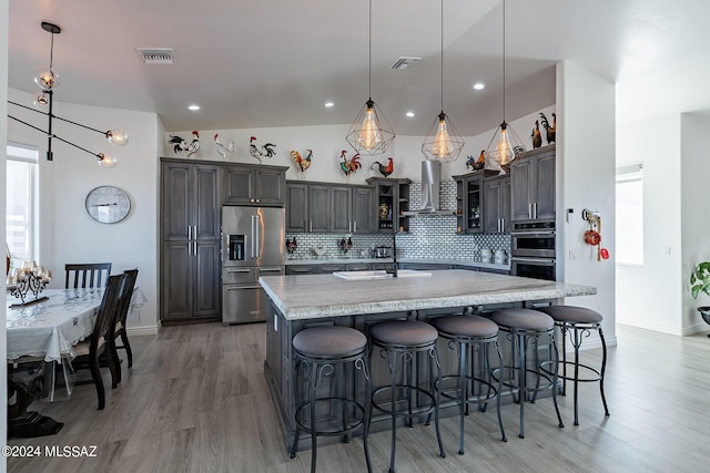 kitchen with visible vents, wall chimney exhaust hood, appliances with stainless steel finishes, a sink, and backsplash