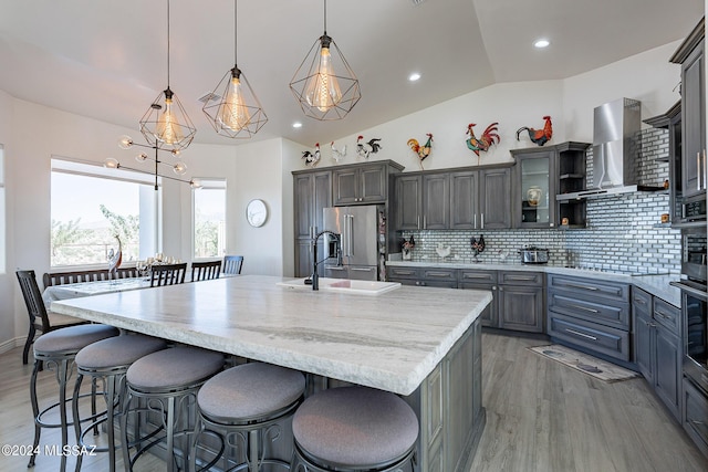 kitchen with high end fridge, backsplash, light wood-style floors, a sink, and wall chimney exhaust hood