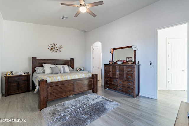 bedroom featuring light wood finished floors, visible vents, arched walkways, baseboards, and lofted ceiling