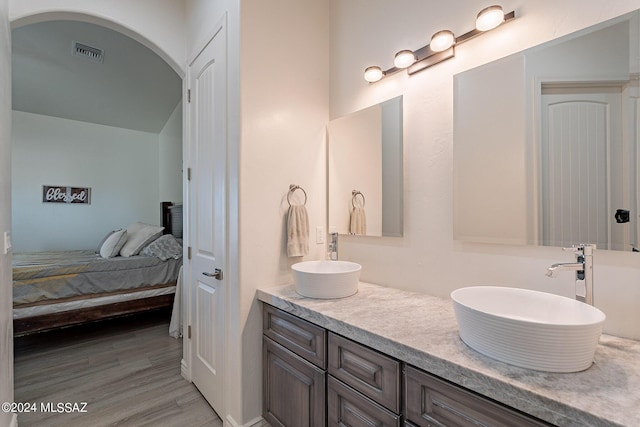 bathroom with double vanity, visible vents, connected bathroom, wood finished floors, and a sink