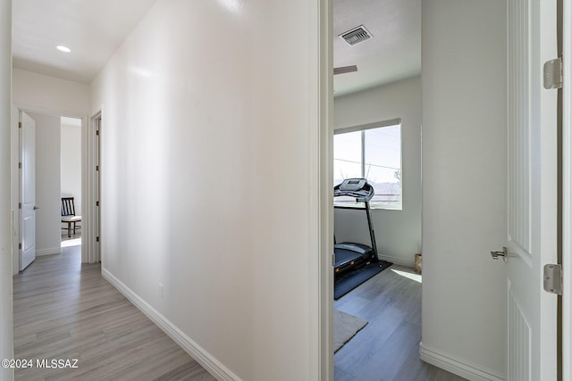 hall with light wood finished floors, visible vents, and baseboards