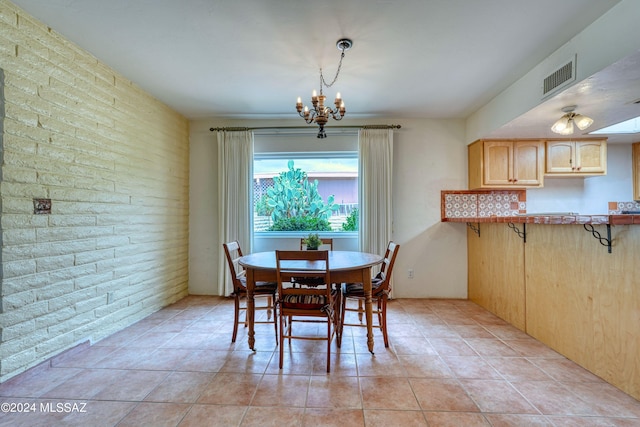 dining space featuring light tile patterned floors, an inviting chandelier, and brick wall