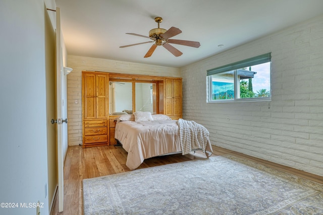 bedroom with ceiling fan, light hardwood / wood-style floors, and brick wall