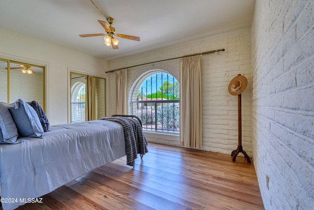 bedroom featuring ceiling fan, wood-type flooring, and brick wall