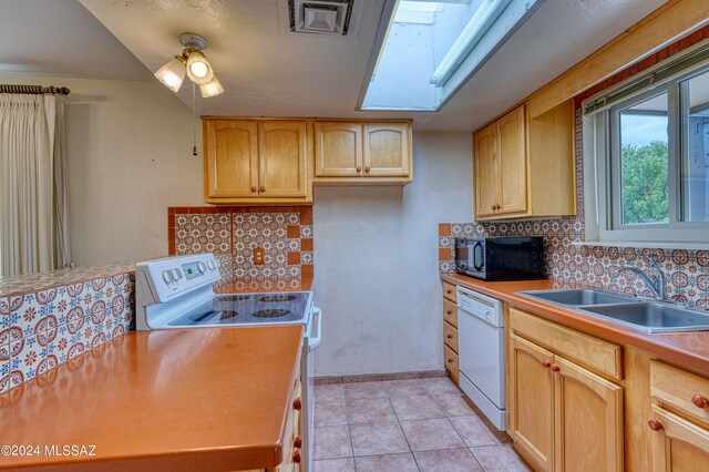 kitchen featuring a skylight, white appliances, light tile patterned floors, and decorative backsplash