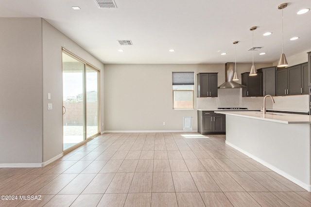 kitchen with a wealth of natural light, tasteful backsplash, wall chimney range hood, and decorative light fixtures