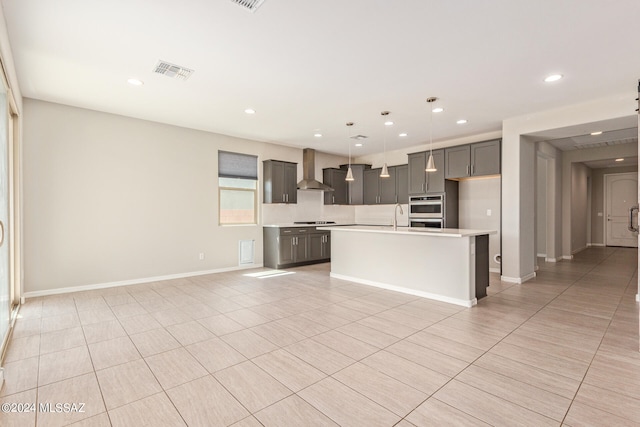 kitchen with wall chimney exhaust hood, hanging light fixtures, light tile patterned flooring, a center island with sink, and double oven