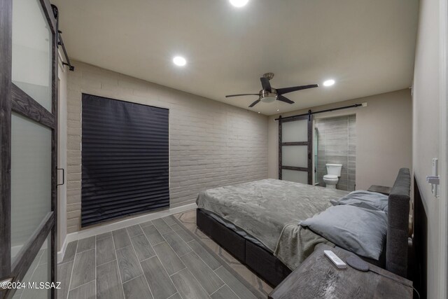 bedroom with ceiling fan, a barn door, wood-type flooring, and ensuite bathroom