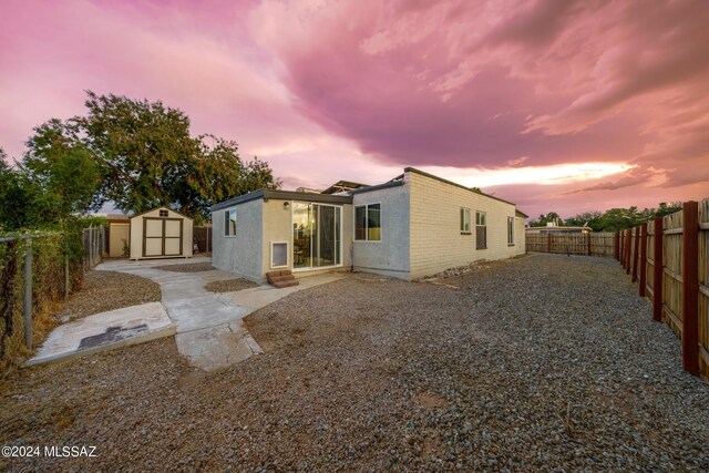 back house at dusk featuring a storage shed and a patio