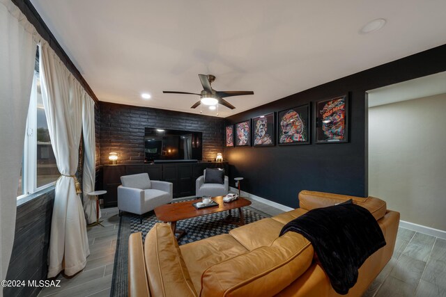 living room featuring ceiling fan, hardwood / wood-style floors, and brick wall