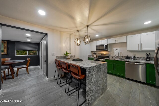 kitchen featuring light hardwood / wood-style flooring, a breakfast bar, green cabinetry, white cabinetry, and appliances with stainless steel finishes