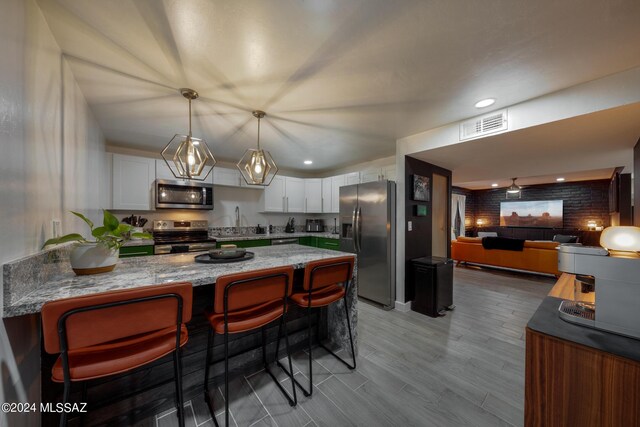 kitchen featuring appliances with stainless steel finishes, white cabinetry, brick wall, light stone countertops, and a kitchen breakfast bar