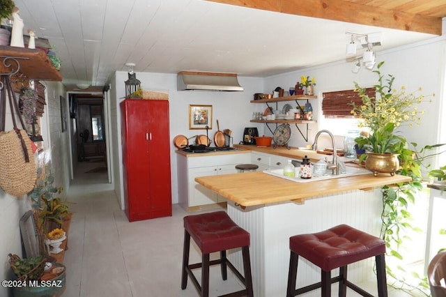 kitchen featuring wood counters, sink, white cabinetry, a kitchen bar, and kitchen peninsula