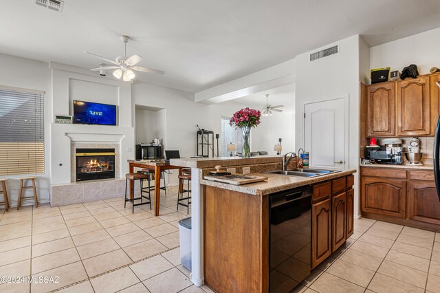 kitchen with dishwasher, light tile patterned flooring, a fireplace, and an island with sink