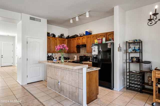 kitchen featuring light tile patterned flooring, backsplash, a kitchen island with sink, and black appliances