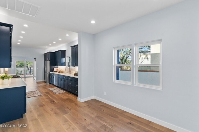 kitchen with stainless steel fridge, sink, light wood-type flooring, and backsplash