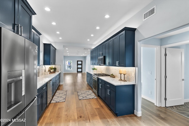 kitchen featuring blue cabinetry, backsplash, appliances with stainless steel finishes, and light hardwood / wood-style flooring