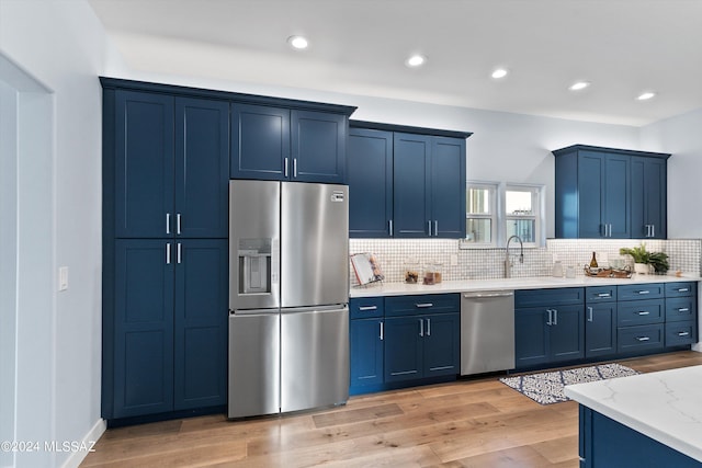 kitchen with stainless steel appliances, blue cabinets, light hardwood / wood-style floors, and light stone counters