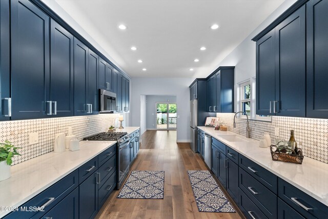 kitchen with appliances with stainless steel finishes, dark hardwood / wood-style flooring, tasteful backsplash, sink, and blue cabinetry