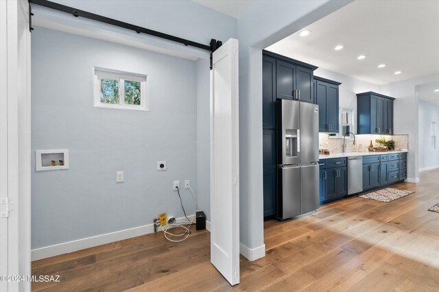 kitchen with backsplash, stainless steel appliances, sink, blue cabinetry, and a barn door