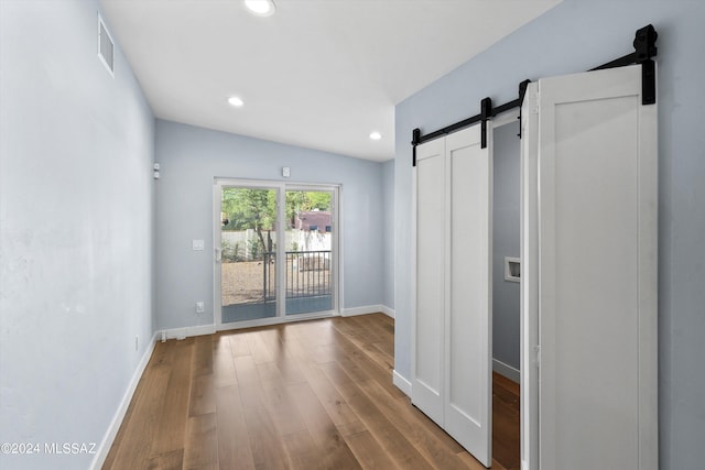 interior space with a barn door, hardwood / wood-style flooring, and vaulted ceiling