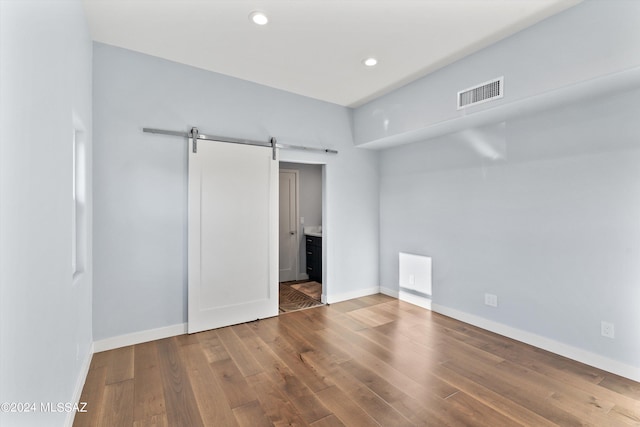 unfurnished bedroom featuring wood-type flooring, a barn door, and connected bathroom