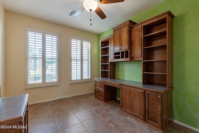 unfurnished office with ceiling fan, built in desk, and light tile patterned floors